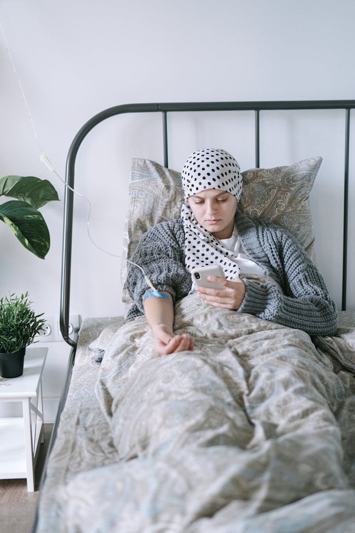 A woman undergoing chemotherapy relaxes in a hospital bed, using her phone for support.