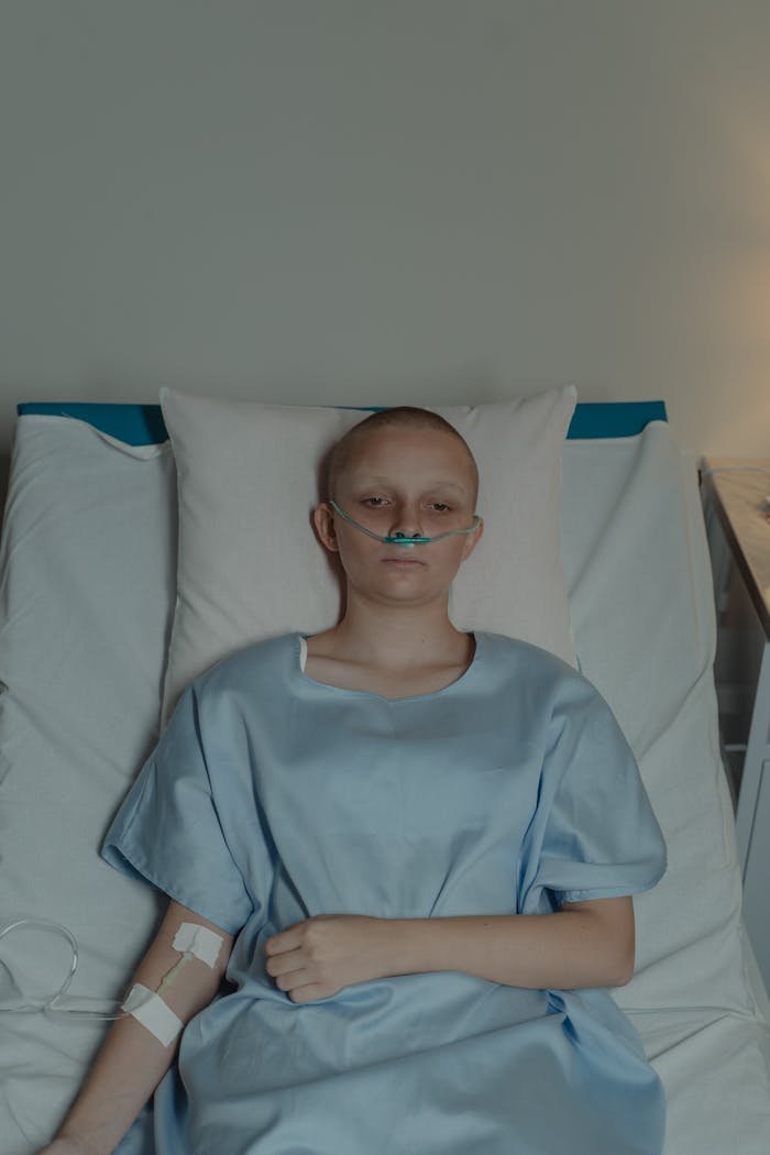 Bald woman in hospital gown with nasal cannula, representing sickness and recovery.