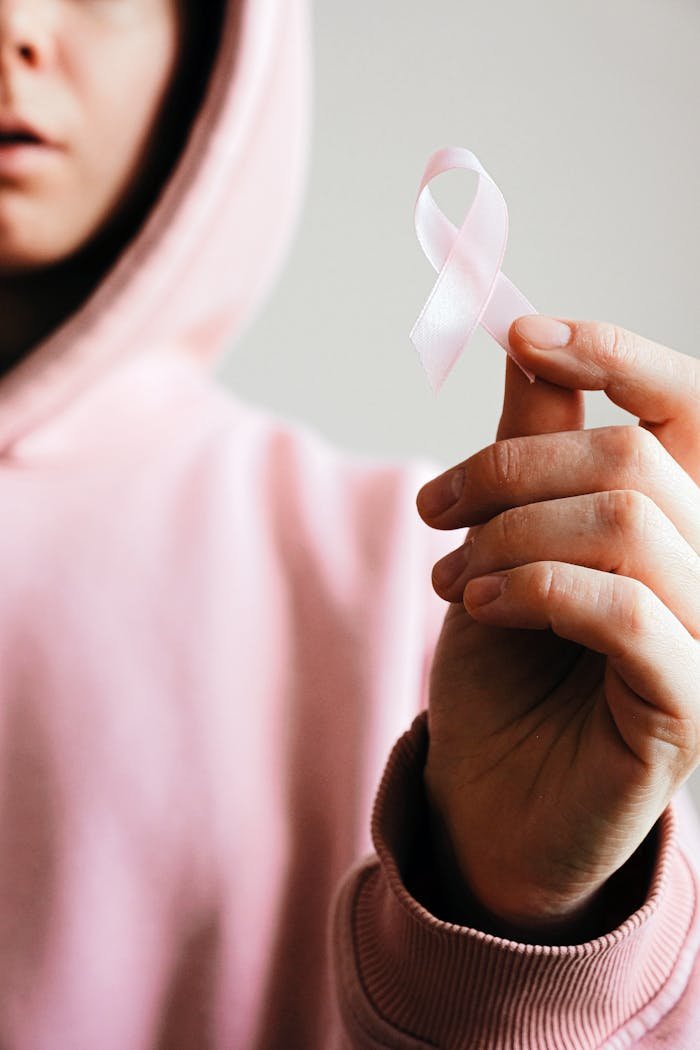Close-up of a person holding a pink ribbon symbolizing breast cancer awareness.